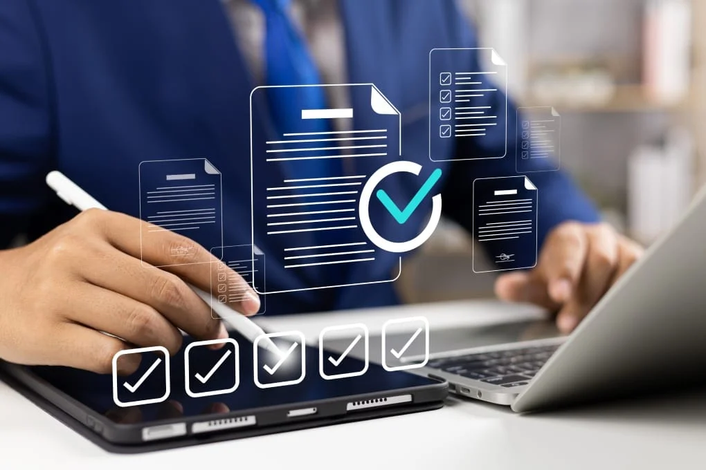 Business person filling out a digital checklist and assessment questionnaire on a laptop and tablet.